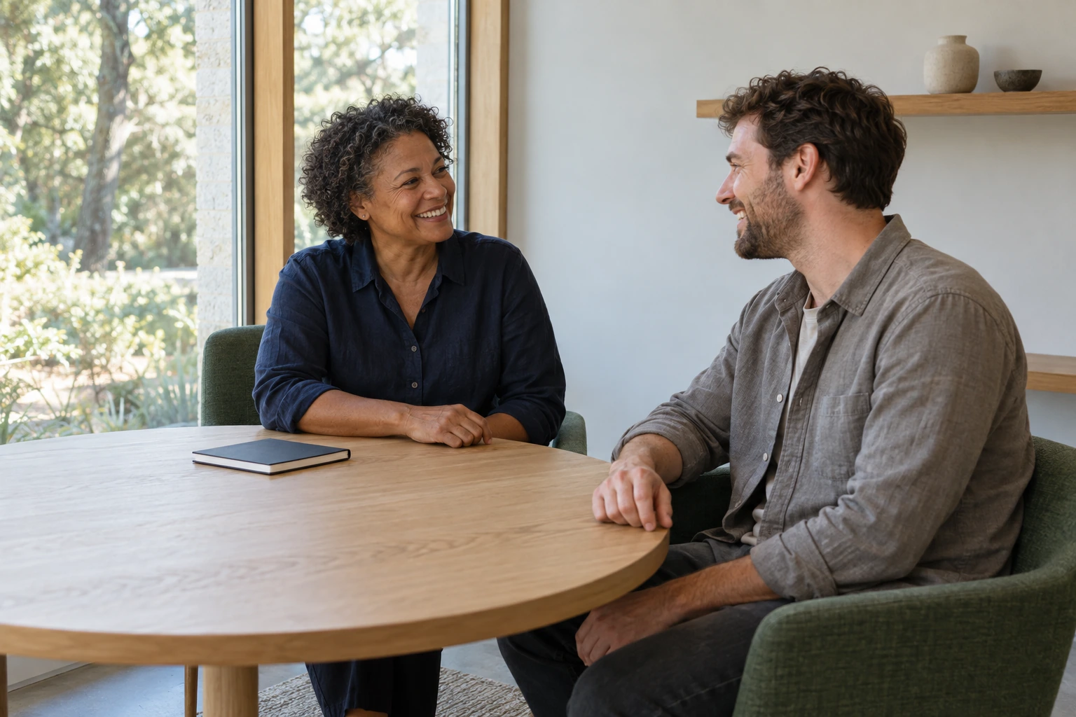 Two adults sharing a relaxed conversation at a round table in a light-filled practice